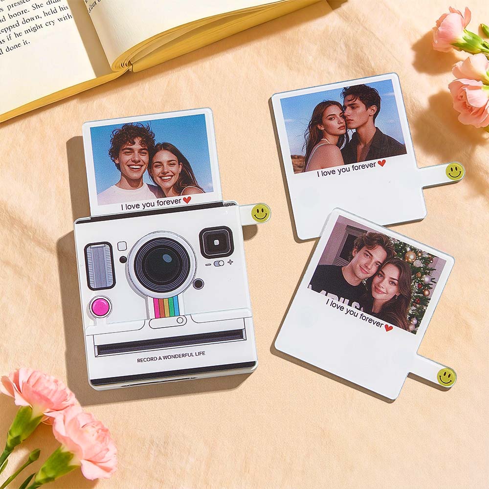 Instant camera with printed photos of a couple on a wooden surface with flowers.
