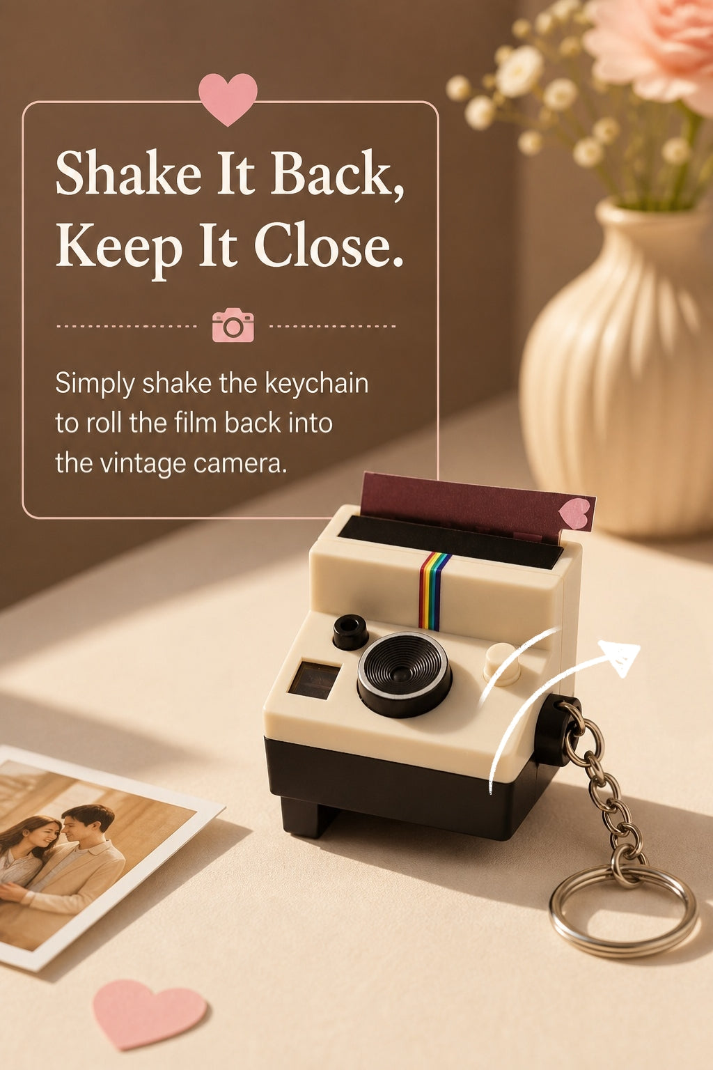 A miniature vintage instant camera keychain sits on a beige tabletop with a small printed photo and pink heart props nearby. Text on the left reads, 'Shake It Back, Keep It Close.