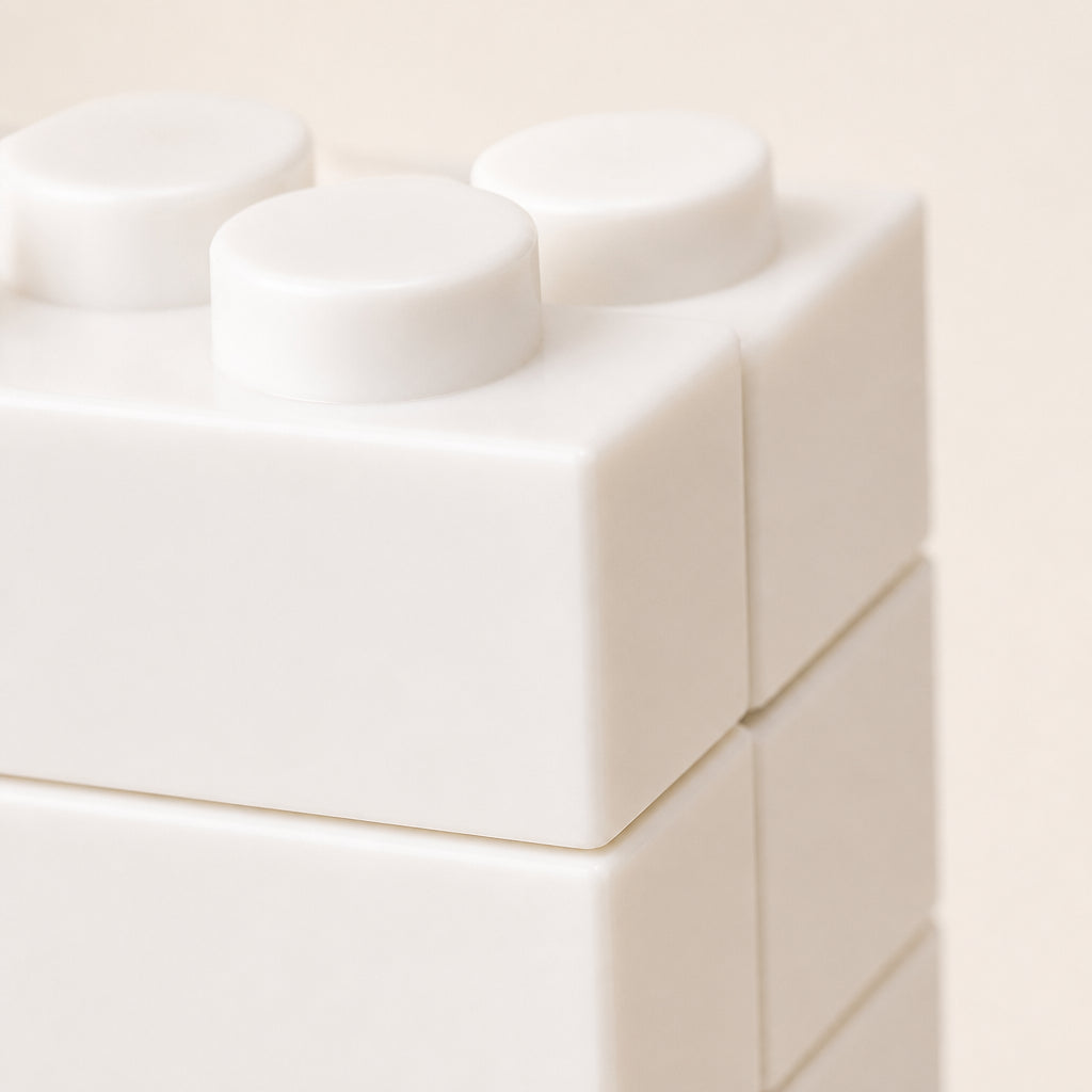 Close-up of a white modular block toy with rounded square shapes and circular studs, photographed against a warm off-white background.