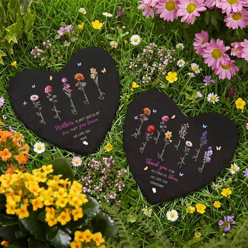 Two heart-shaped black plaques with floral designs and text on a grassy background with flowers.