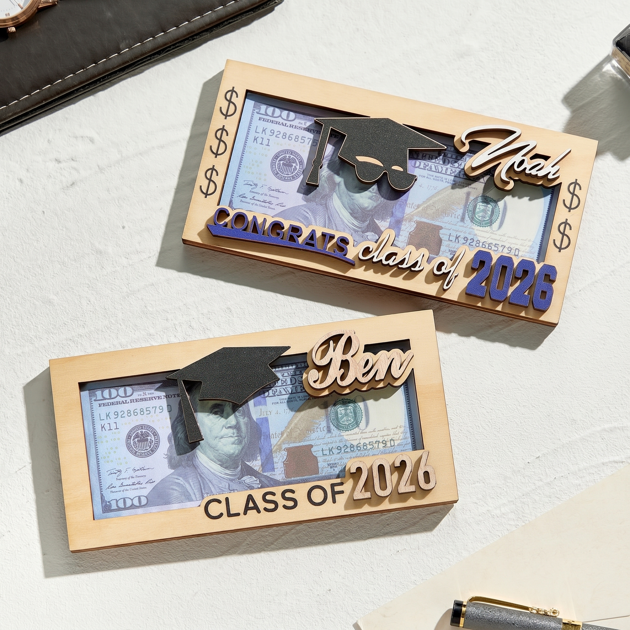 Two wooden money clip awards with graduation-themed designs on a light surface.